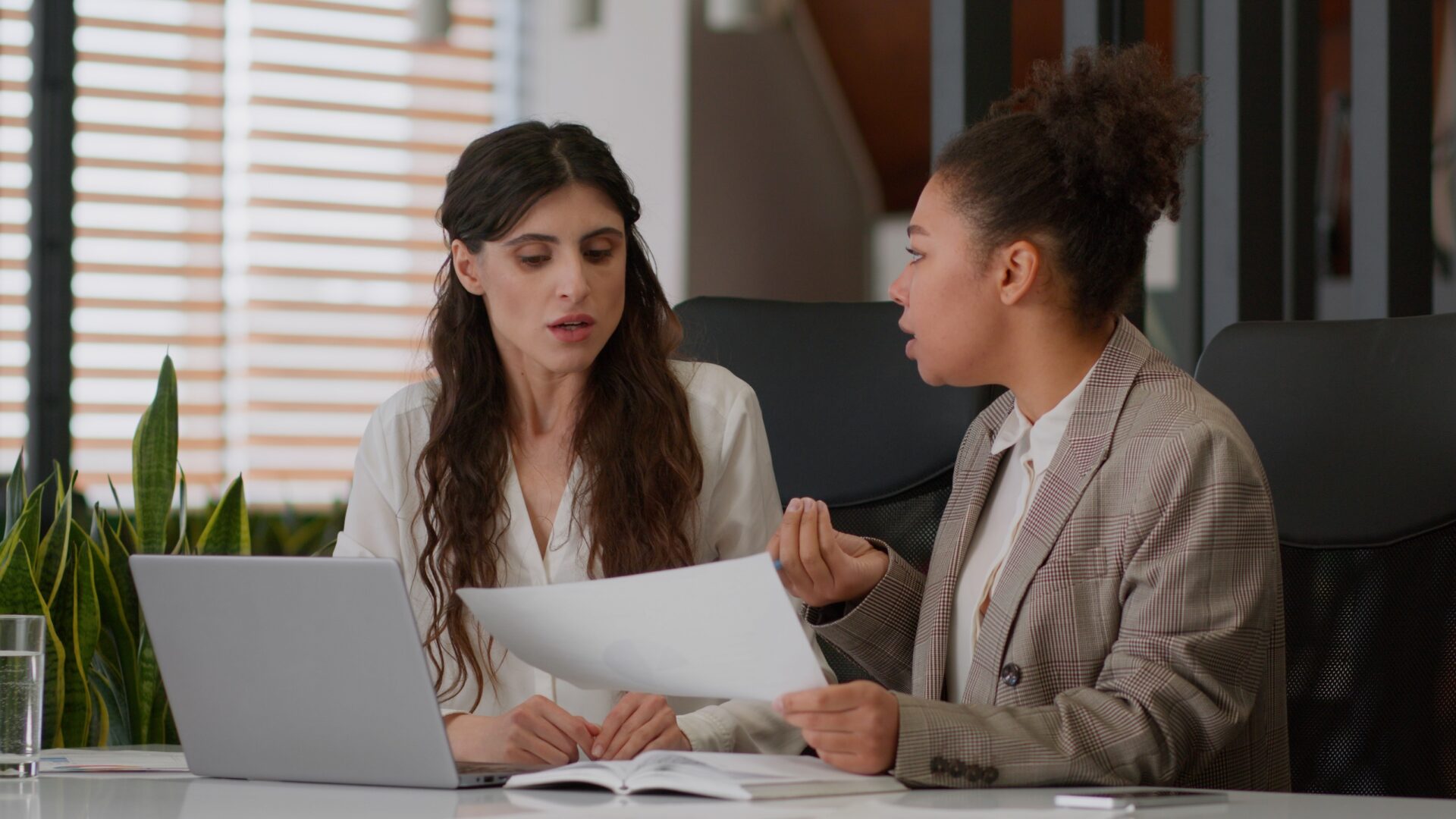Two people seated at a desk reviewing printed documents together, with a laptop open beside them