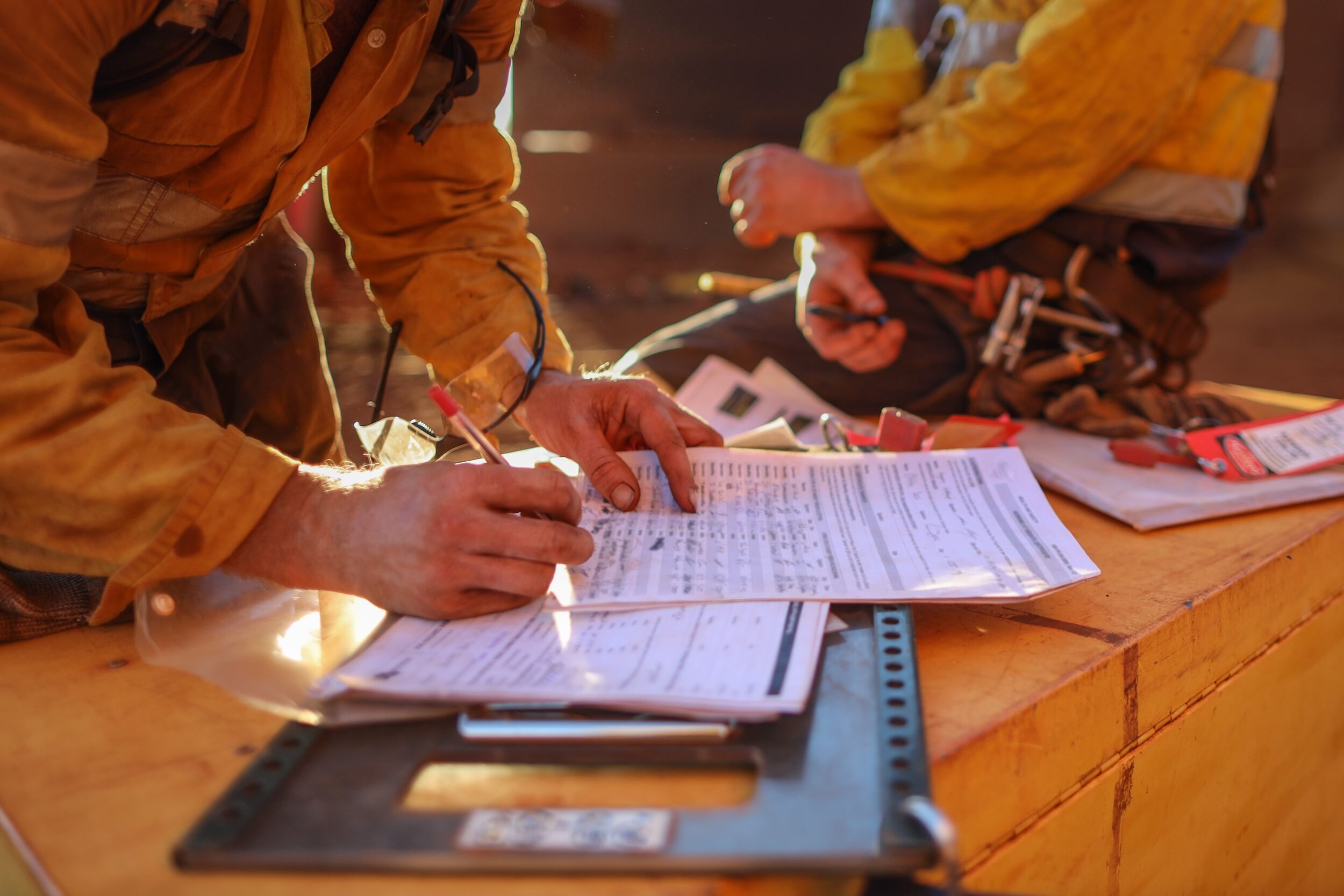 Worker in protective clothing filling out paperwork on a clipboard while seated on a worksite surface
