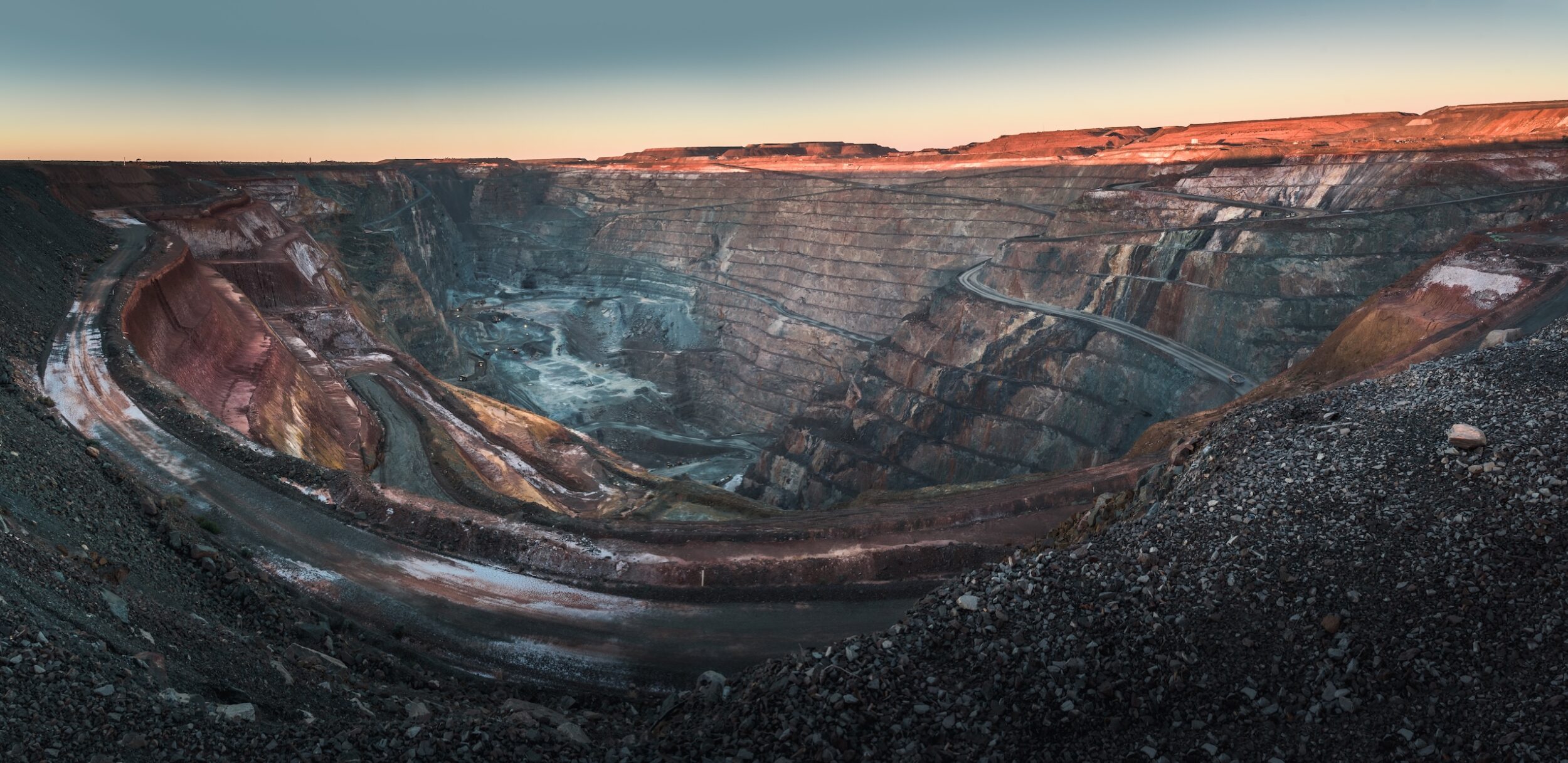Wide view of a large open-pit mine with layered rock walls and winding access roads under a clear sky