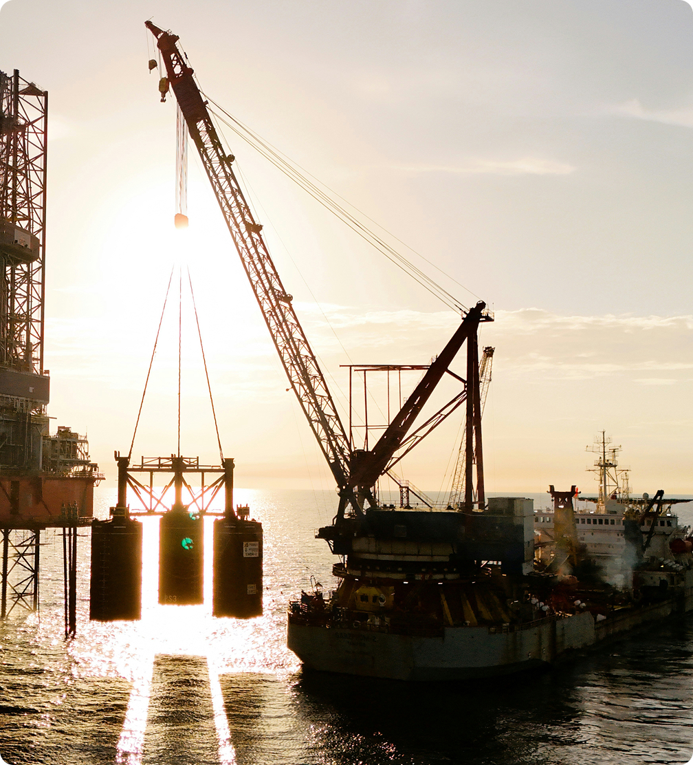 Crane vessel lifting large equipment beside an offshore platform on the ocean at sunset