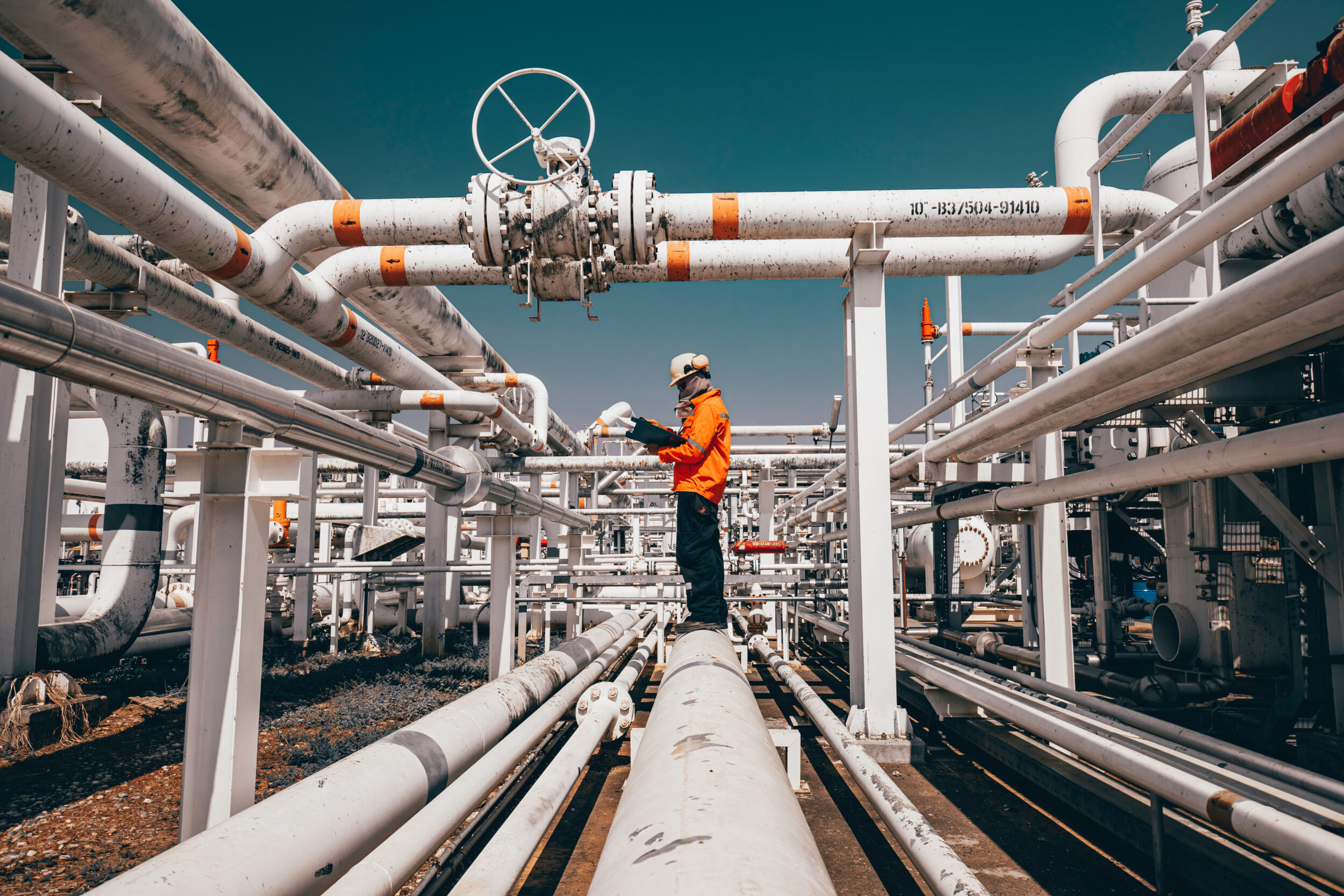 Top view male worker inspection at steel long pipes and pipe elbow in station oil factory during refinery valve of visual check record pipeline oil and gas industry