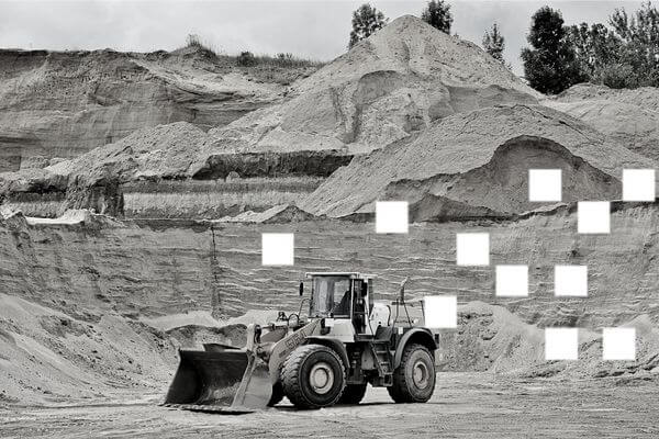 Front loader operating at a sand quarry with large piles of excavated material visible in the background.