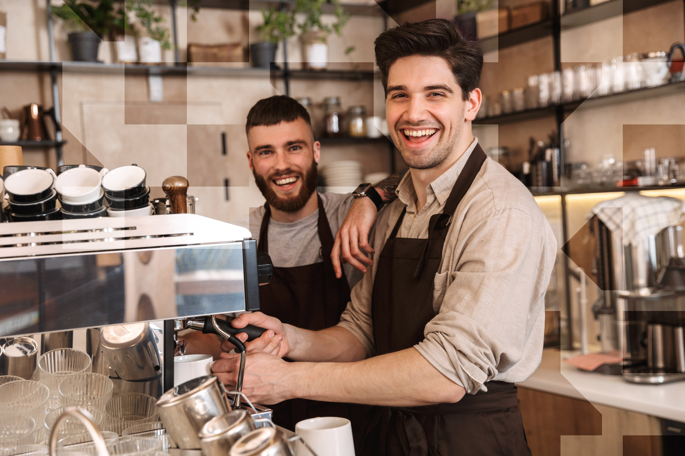 Two café workers standing behind a counter, smiling while operating a coffee machine indoors