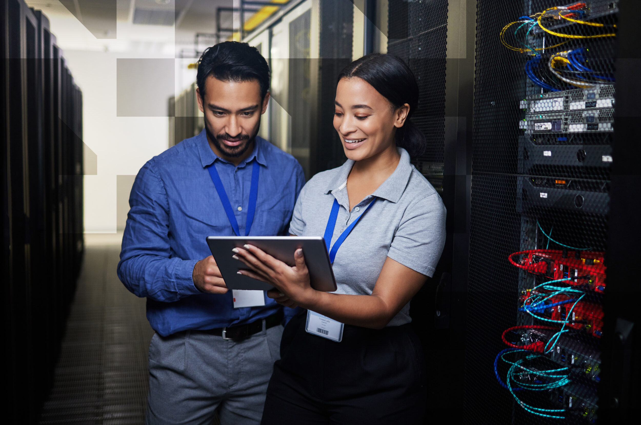 Two people standing between server racks indoors, looking at a tablet while discussing equipment