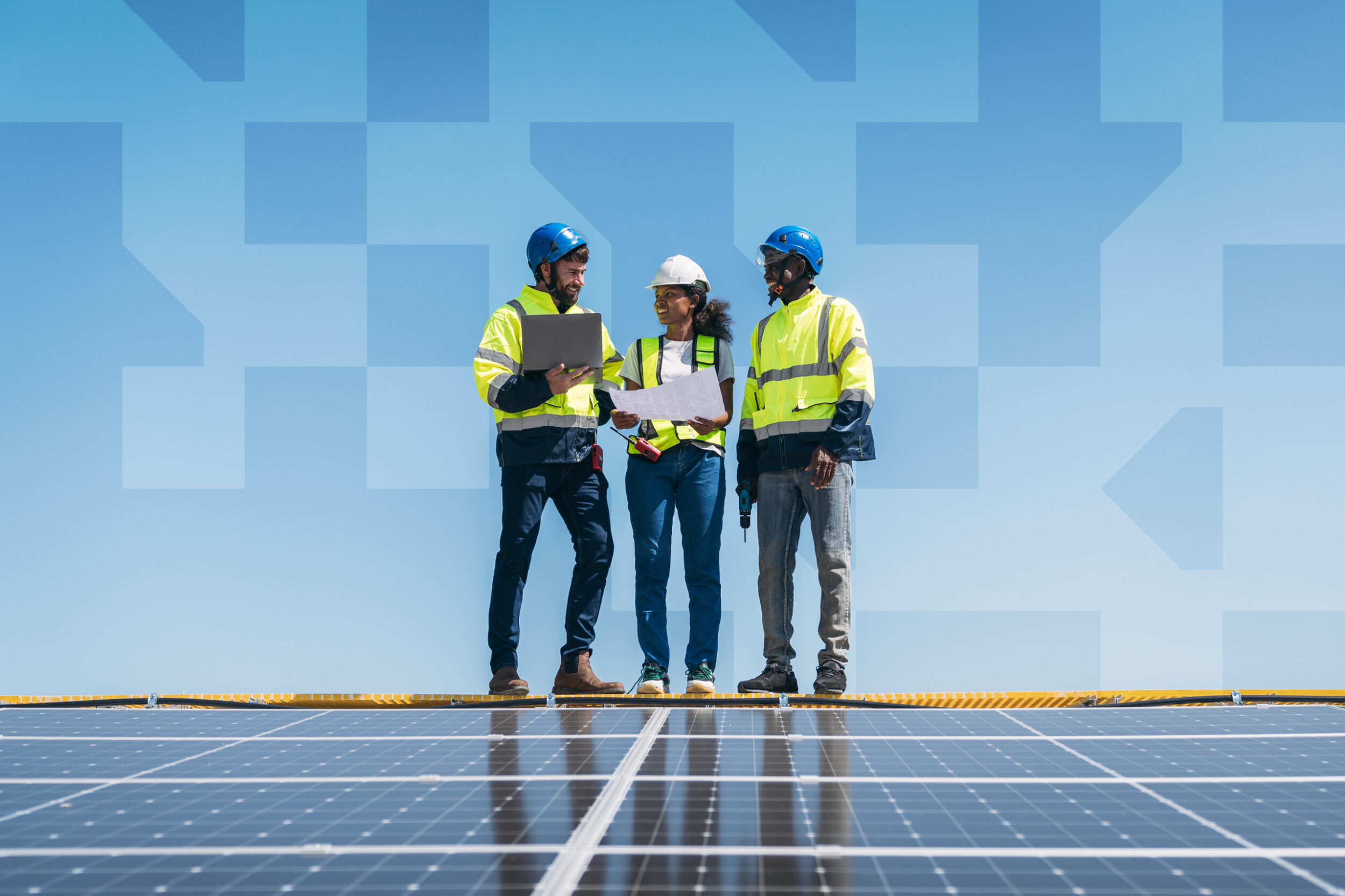 Three people wearing safety helmets and vests standing outdoors while reviewing documents together