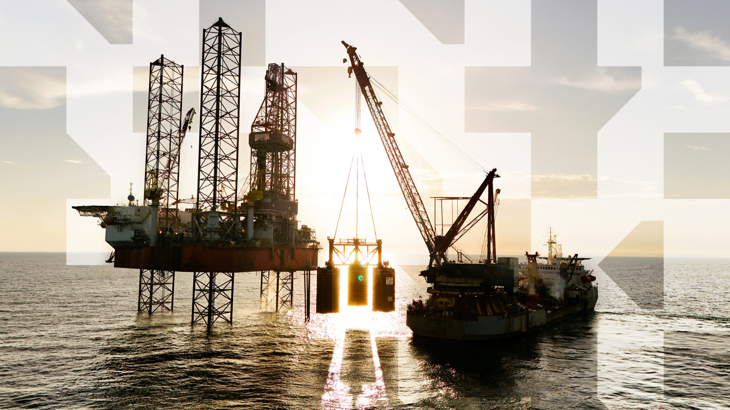 Offshore drilling platform with crane vessel lifting equipment at sea during sunset industrial operations